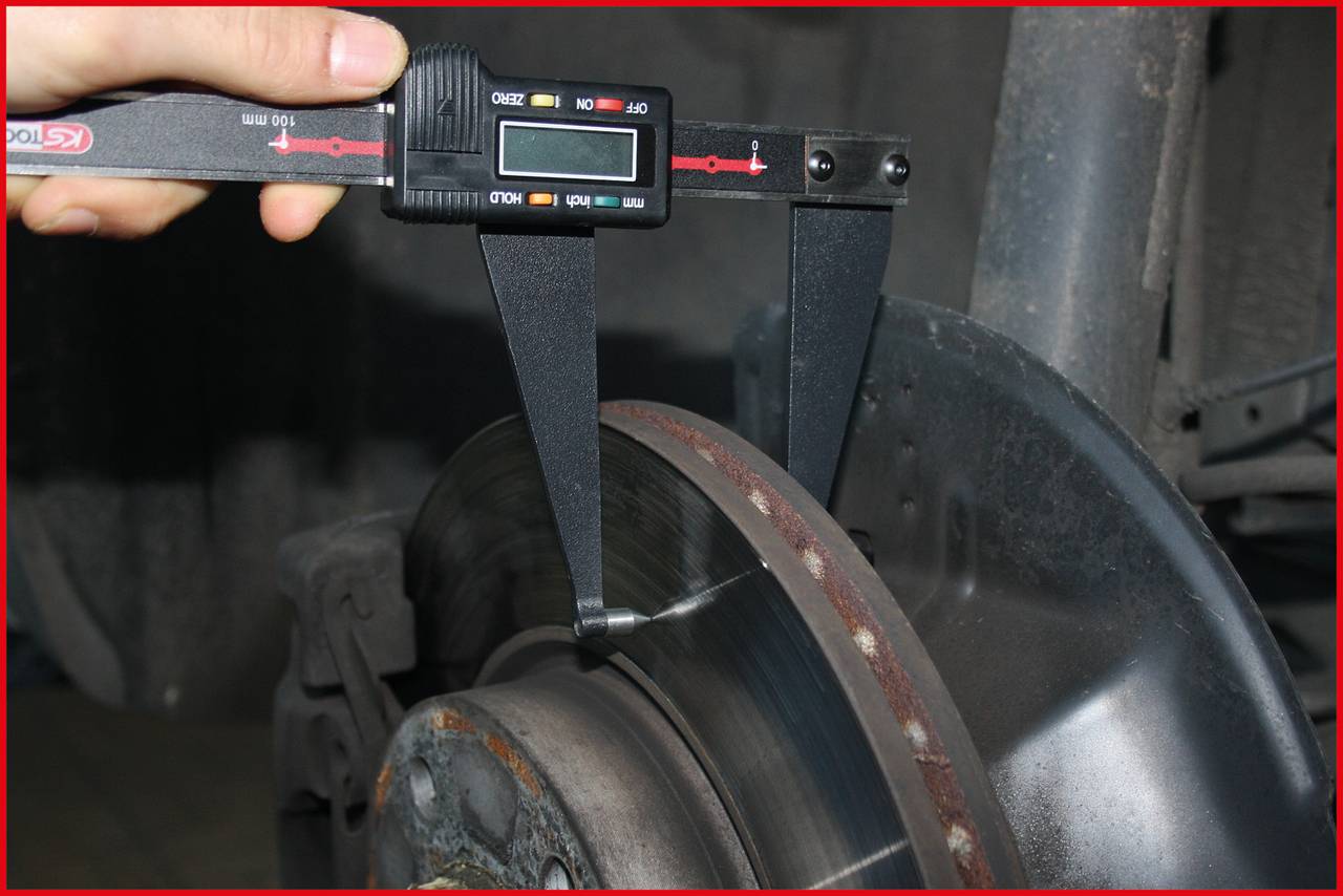 Eine Hand misst die Dicke einer Bremsscheibe mit einer digitalen Bremsscheiben-Mikrometerlehre in einer Werkstatt.