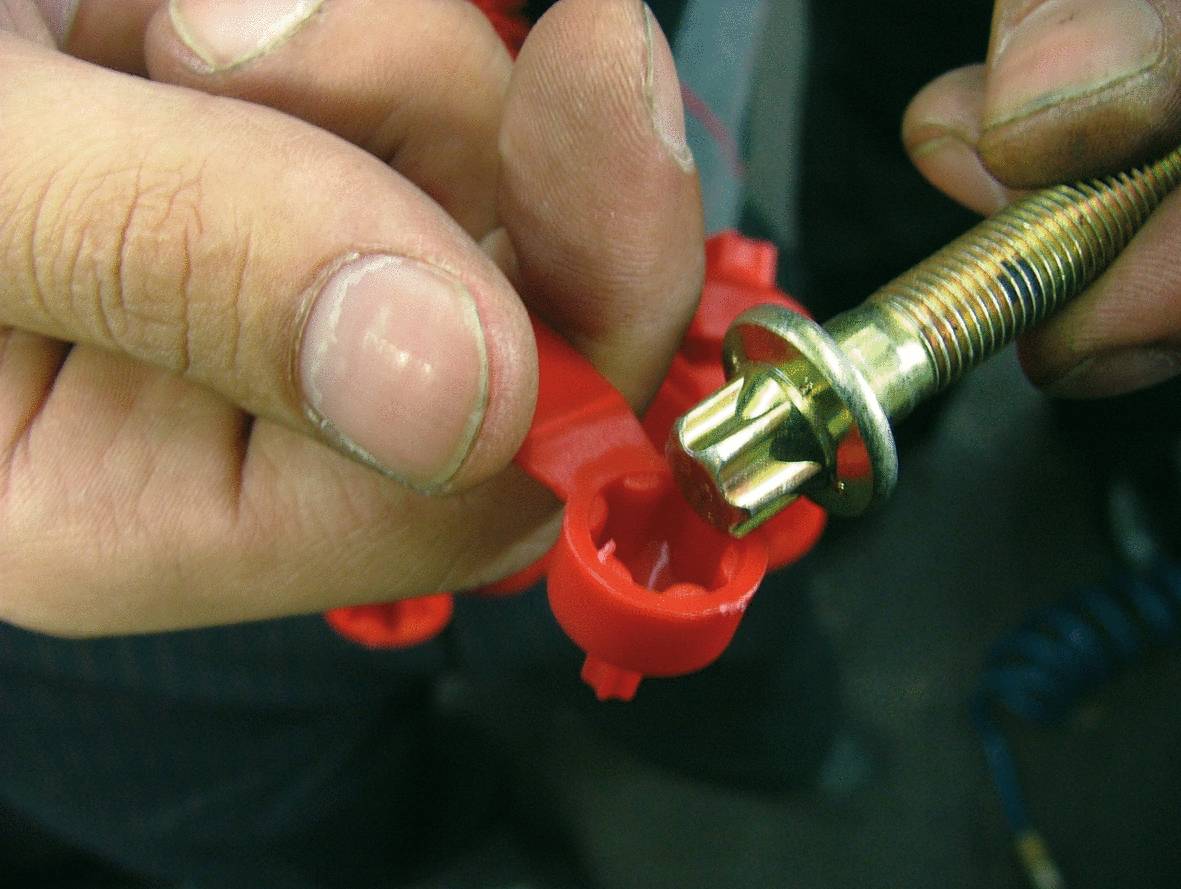 Eine Hand befestigt eine rote Kunststoffklemme an einem metallenen Schraubenelement.