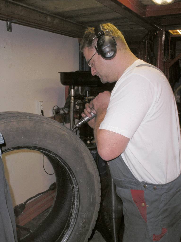 Ein Mechaniker mit Kopfhörern bearbeitet einen Autoreifen in einer Werkstatt.