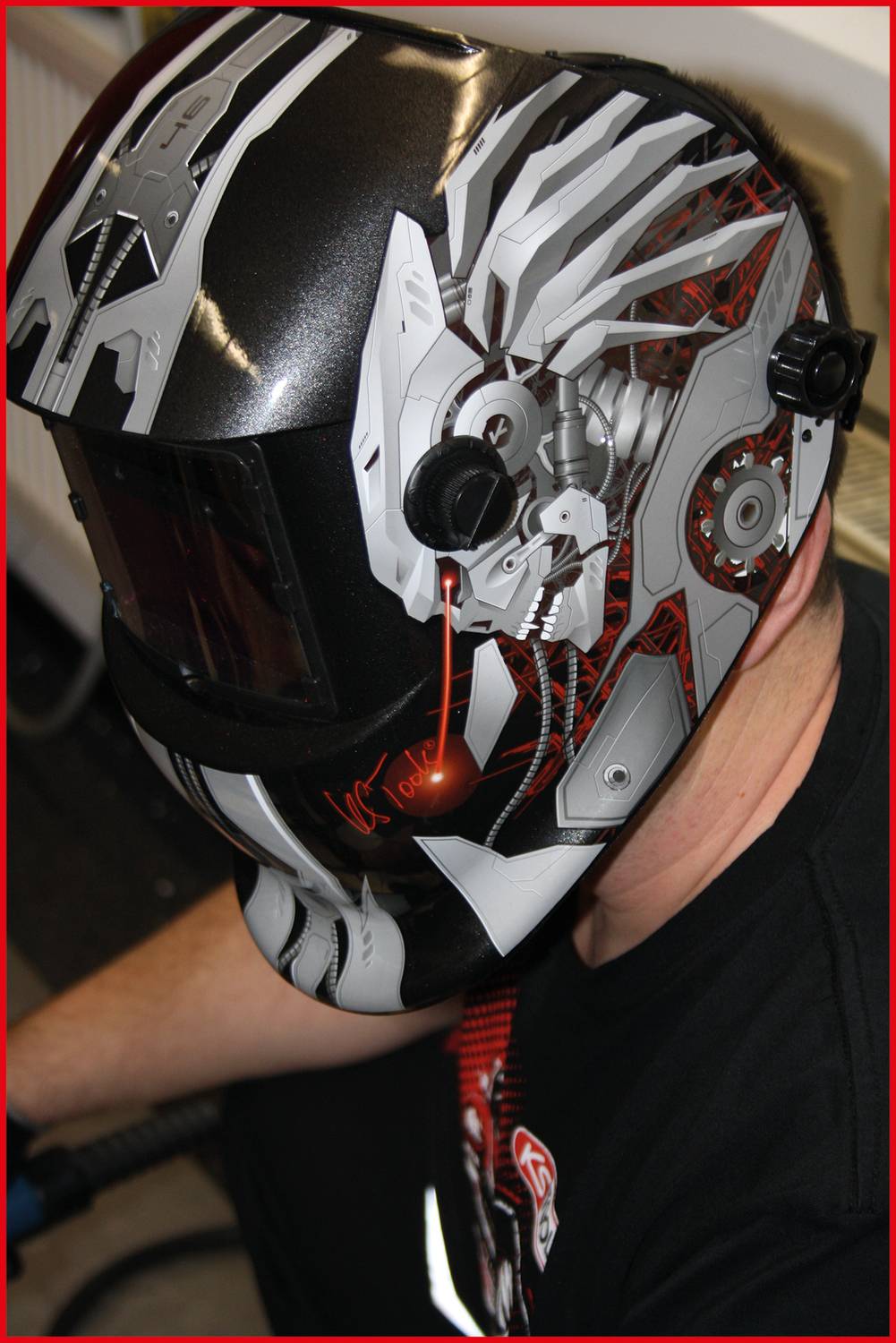 Person mit kunstvollem Schweißhelm in modernem Design, zeigt Details von Maschinenelementen und Schädel.