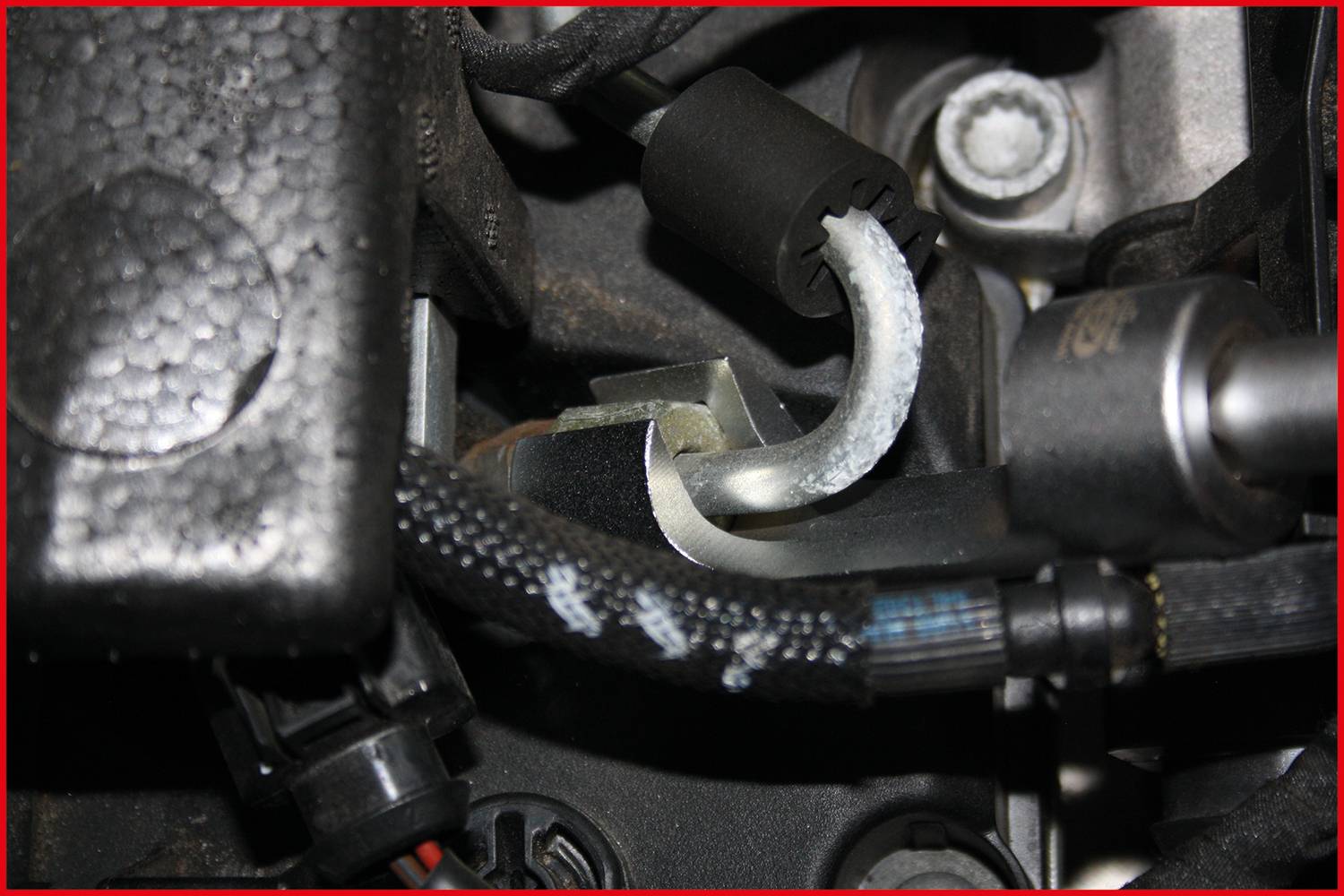 Ein Nahaufnahme eines Motorenteils, das Rohre und Kabel zeigt, umgeben von Kunststoff- und Metallkomponenten. Keine spezifische Handlung erkennbar.