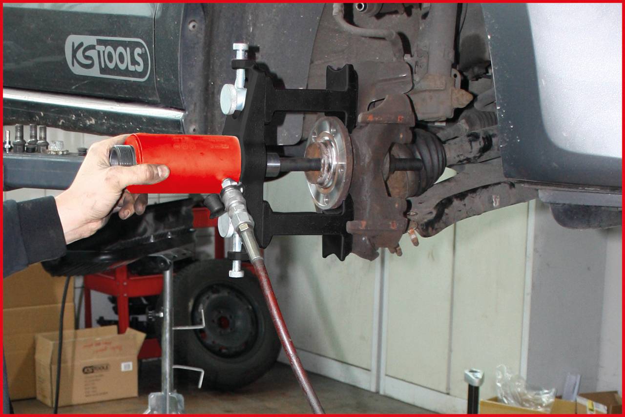 Eine Person benutzt ein hydraulisches Werkzeug, um eine Bremsscheibe an einem Auto zu entfernen. Der Fokus liegt auf der Mechanik.