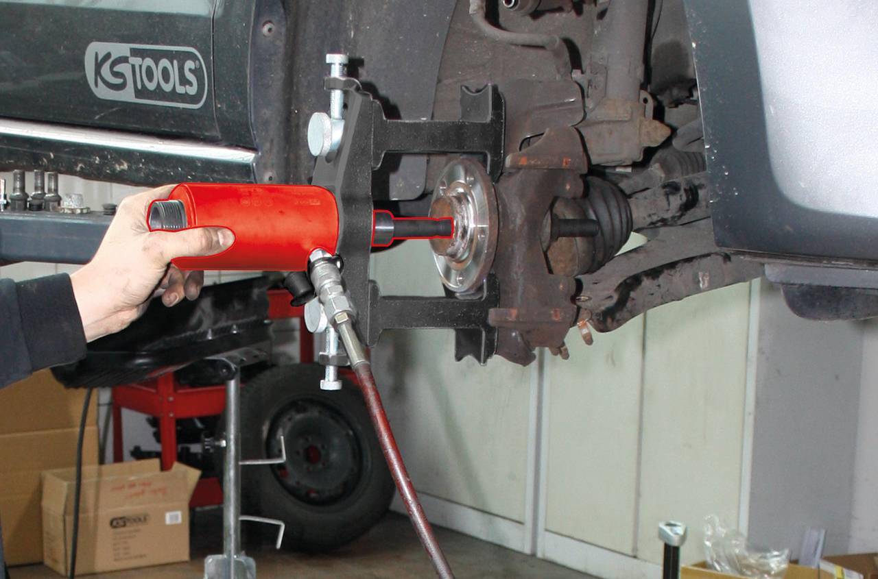 Eine Hand führt mit einem pneumatischen Bremsenentlüftungsgerät Wartungsarbeiten an der Bremsanlage eines Fahrzeugs im Autowerkstatt durch.
