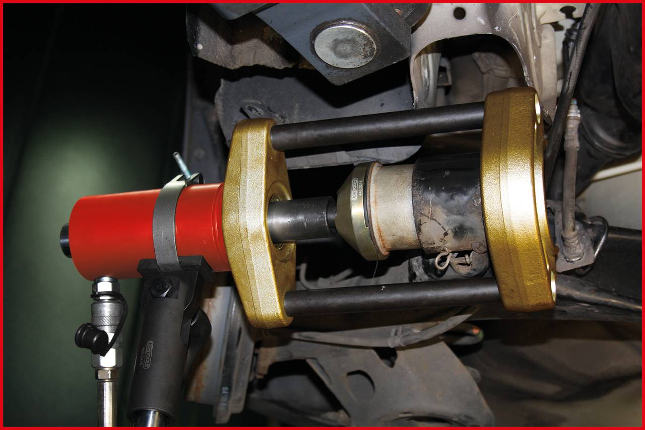Ein hydraulisches Werkzeug entfernt eine Buchse aus einem Fahrzeugaufhängungsteil. Es wird ein roter Hydraulikzylinder verwendet.