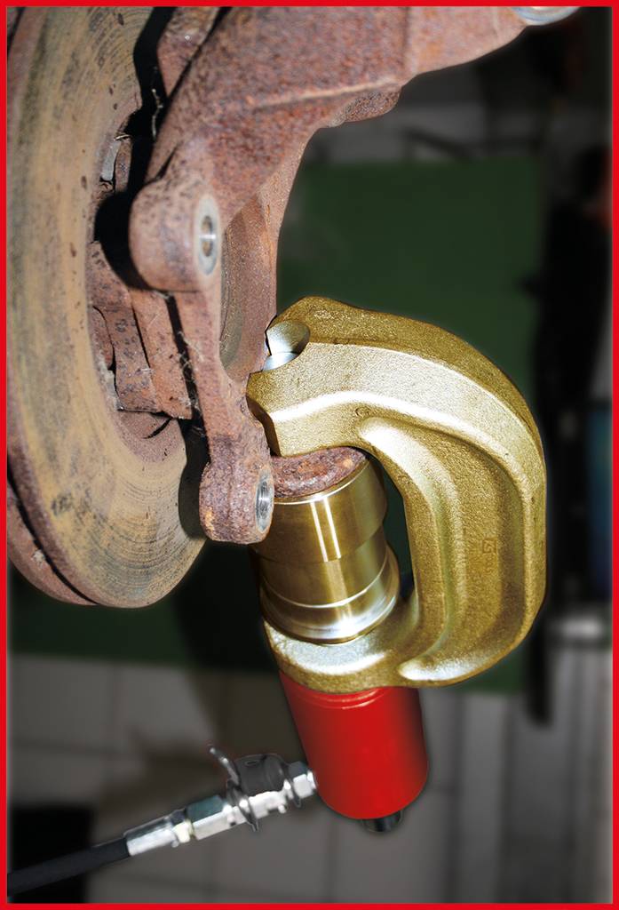 Nahaufnahme eines Bremskolbenrücksetzers, der an einer Bremsscheibe arbeitet. Gerät zeigt rote und goldene Teile. Werkstattumgebung.