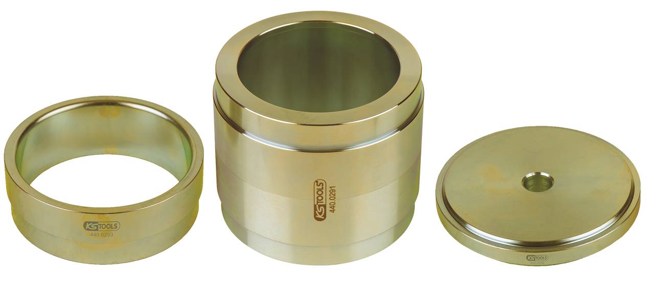 Drei zylindrische Metallteile, eine offene Hülse, ein offener Zylinder und ein flacher Deckel, auf einer weißen Fläche.
