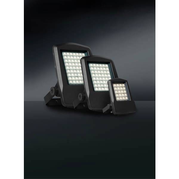 Drei unterschiedlich große, schwarze LED-Flutlichter stehen nebeneinander auf einer dunklen Oberfläche vor einem schwarzen Hintergrund.