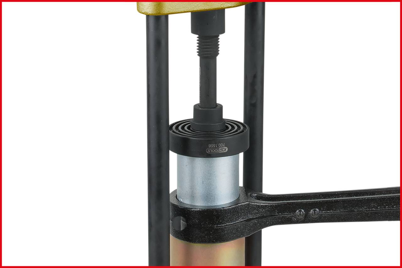Eine hydraulische Presse drückt ein zylinderförmiges Metallteil. Eine Metallstange stabilisiert das Teil.