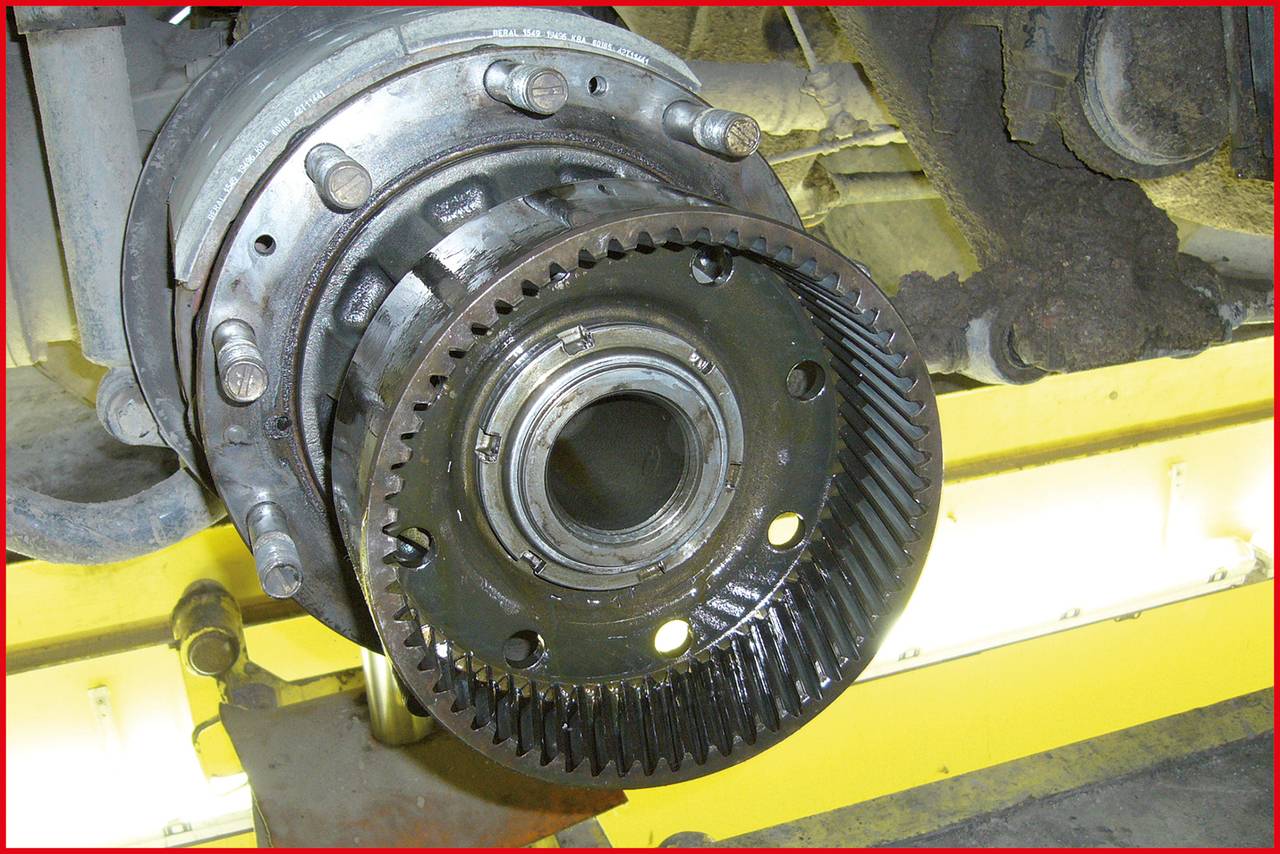 Ansicht einer geöffneten Maschinenkomponente mit Zahnkranz und Bolzen auf einer gelben Unterlage, vermutlich Teil eines Getriebes.