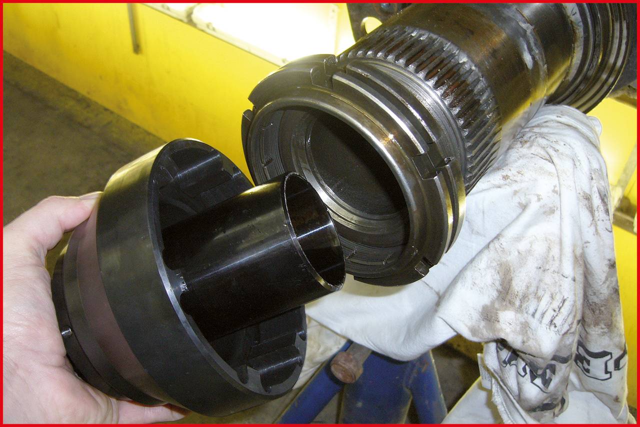 Eine Hand hält ein schwarzes Kunststoffwerkzeug, das von einer Metallwelle getrennt wird. Die Umgebung wirkt industriell.