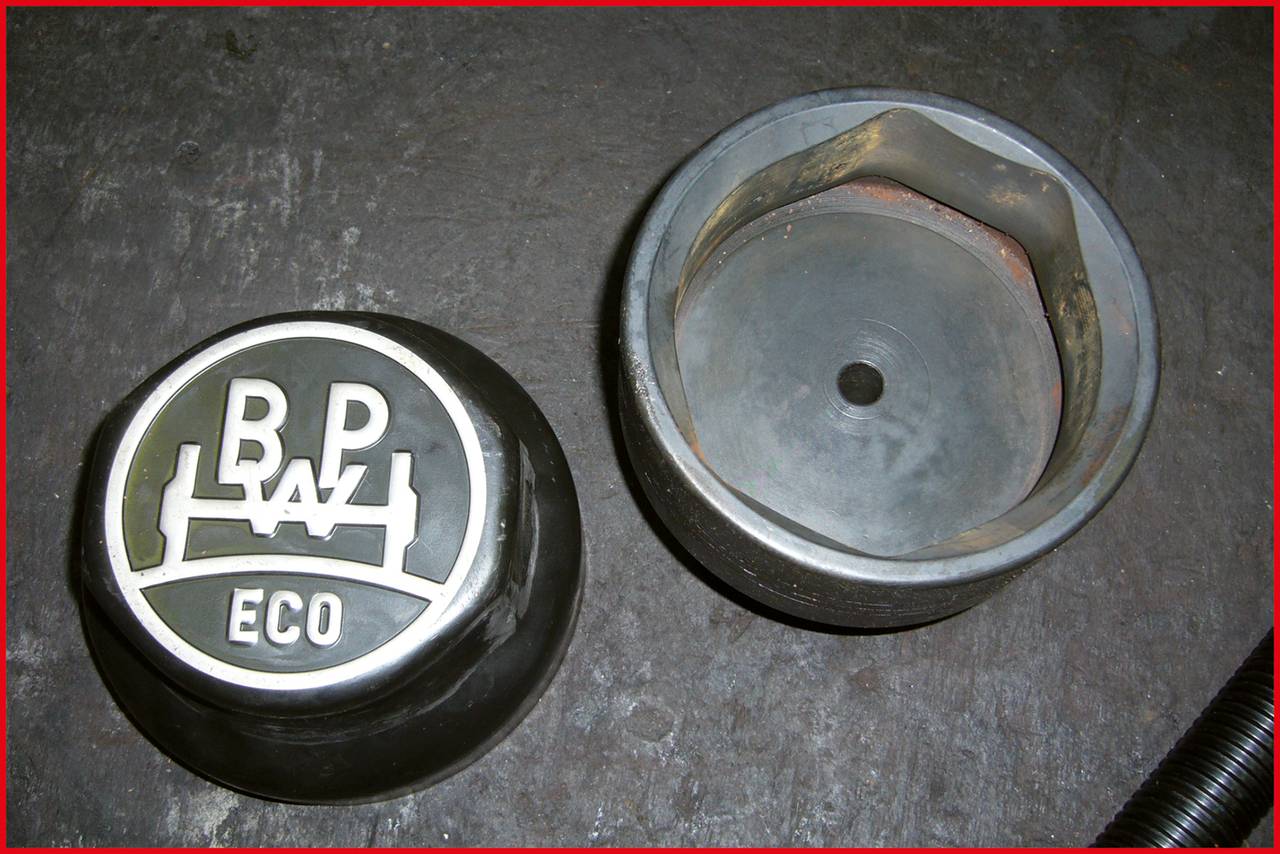 Zwei Metallkomponenten auf einem Betonboden. Links eine Abdeckung mit 'BP ECO'-Logo; rechts die passende Aufnahme ohne Logo.