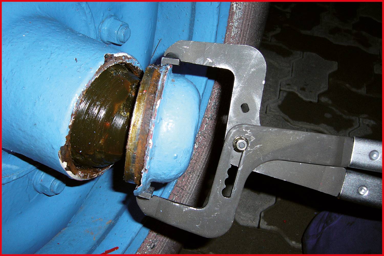 Eine Rohrzange hält ein blaues Metallrohr. Sie zeigt eine mechanische Reparatur oder Wartung.