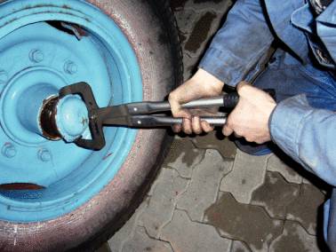 Eine Person in Arbeitskleidung entfernt eine Mutter an einem großen blauen Rad mit Zangen auf einem gefliesten Boden.