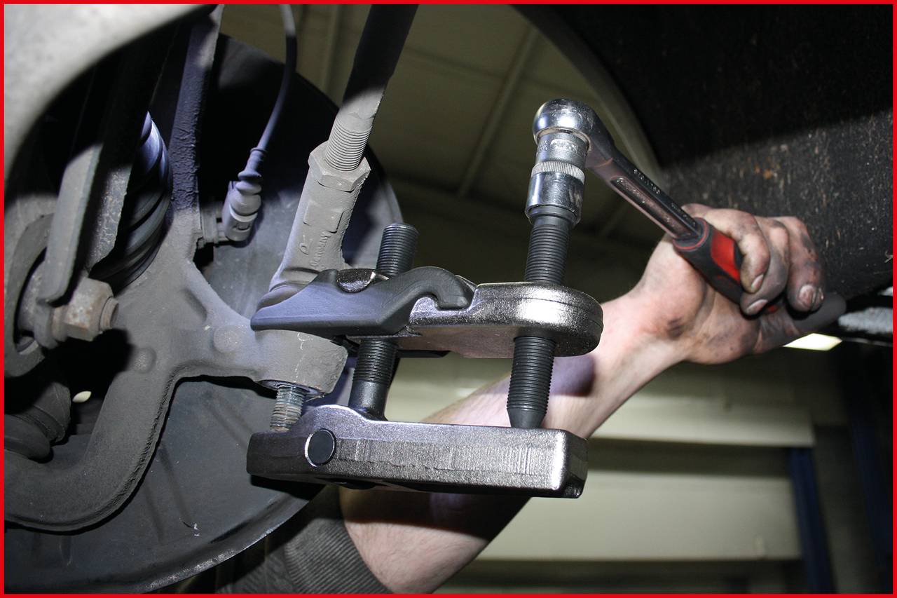 Eine Person repariert Autobremsen, verwendet Schraubenschlüssel und C-Klemme in einer Autowerkstatt. Fokus auf Werkzeugnutzung.