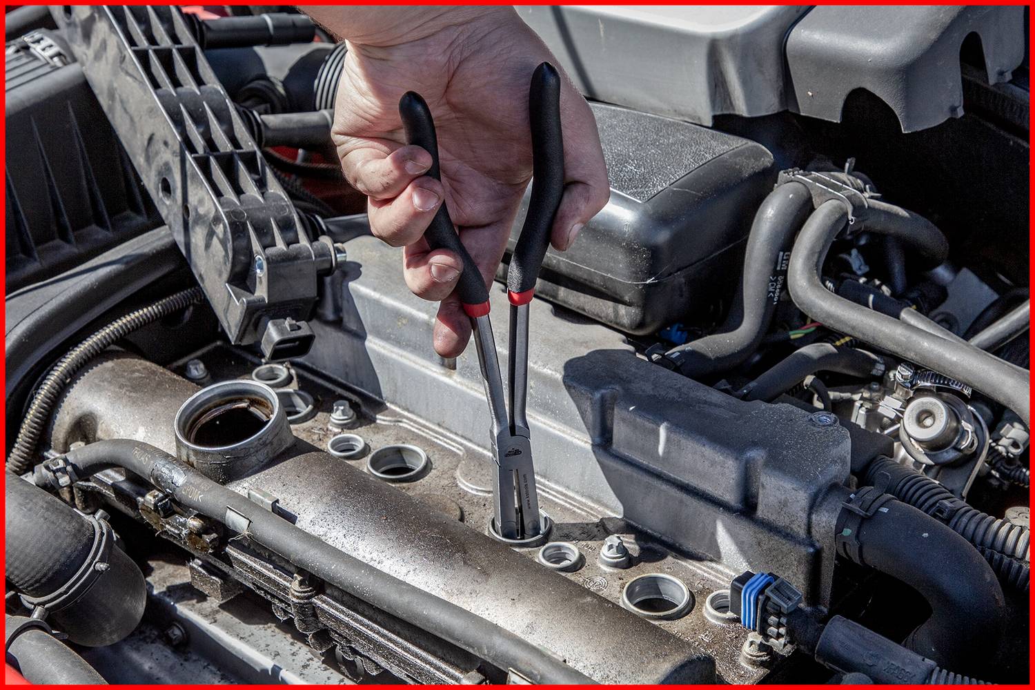 Ein Mechanikerhand hält Zange über einem geöffneten Motorraum, bereit zur Arbeit an Zündkerzen. Einsatz im Kontext Autoreparatur.
