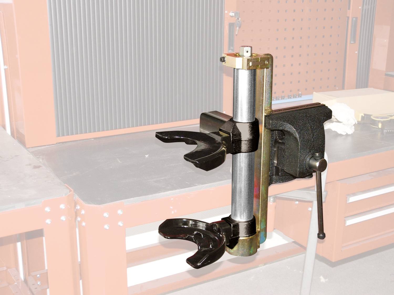 Ein metallisches Werkzeug mit zwei Greifarmen ist an einer Werkbank befestigt. Es dient wahrscheinlich zur Fixierung von Objekten.