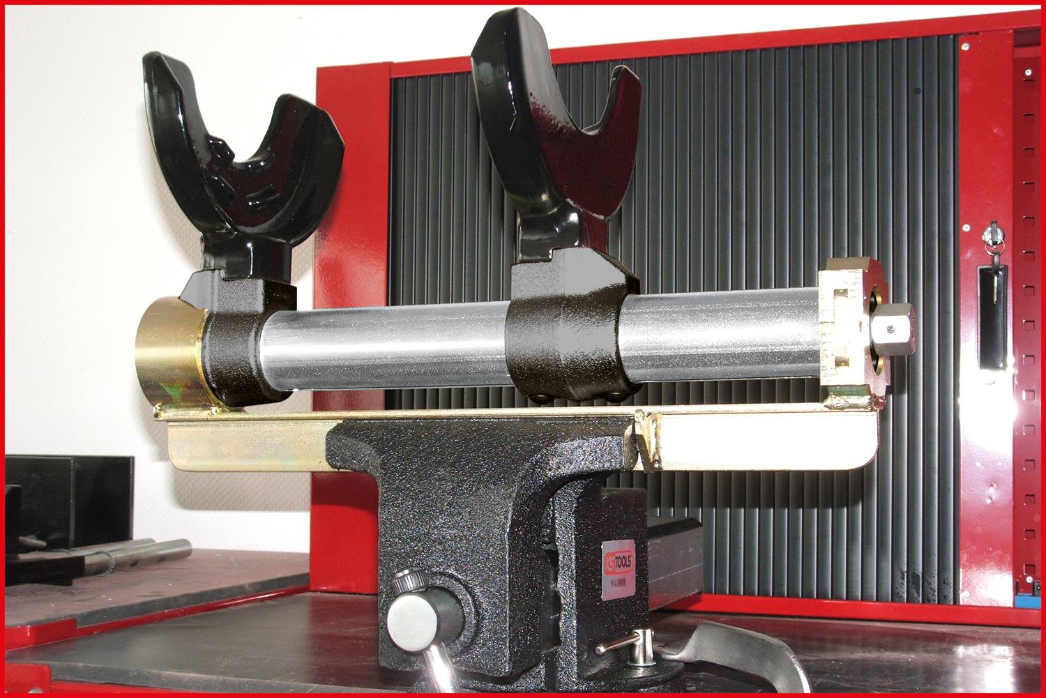 Metallvorrichtung mit zwei schwarzen Klemmen an einem horizontalen Rohr befestigt, ruht auf einem stabilen Sockel vor geriffeltem Hintergrund.