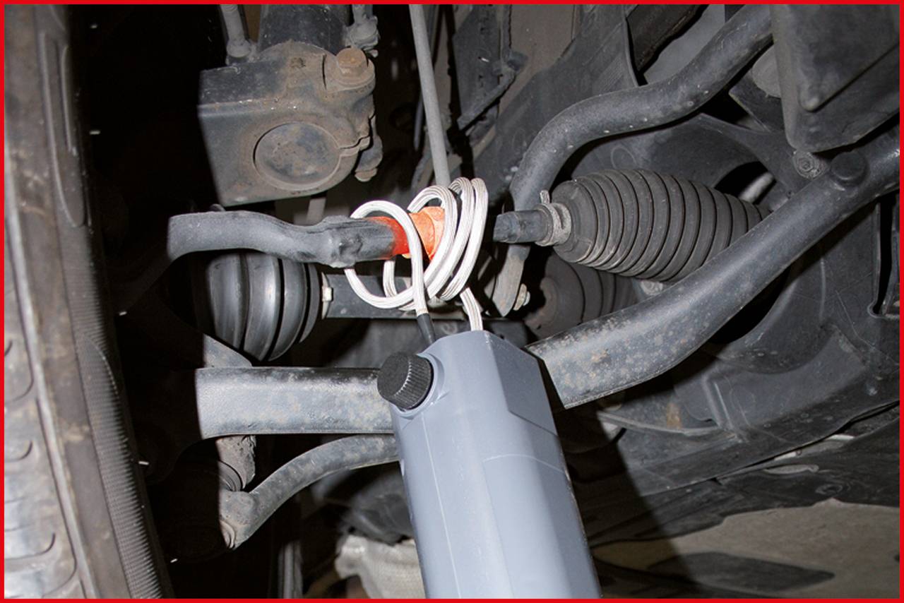 Nahaufnahme eines Autoteils zeigt die Aufhängung und eine reparierte Stelle mit Kabelbindern. Reifen und andere Teile sind sichtbar.