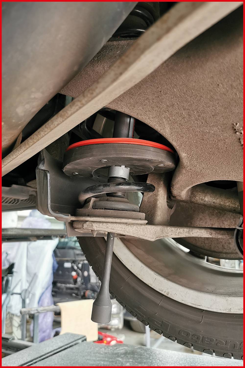 Fahrwerk eines Fahrzeugs auf einer Hebebühne. Sicht auf Stoßdämpfer und Reifen. Umgebung deutet auf eine Werkstatt hin.