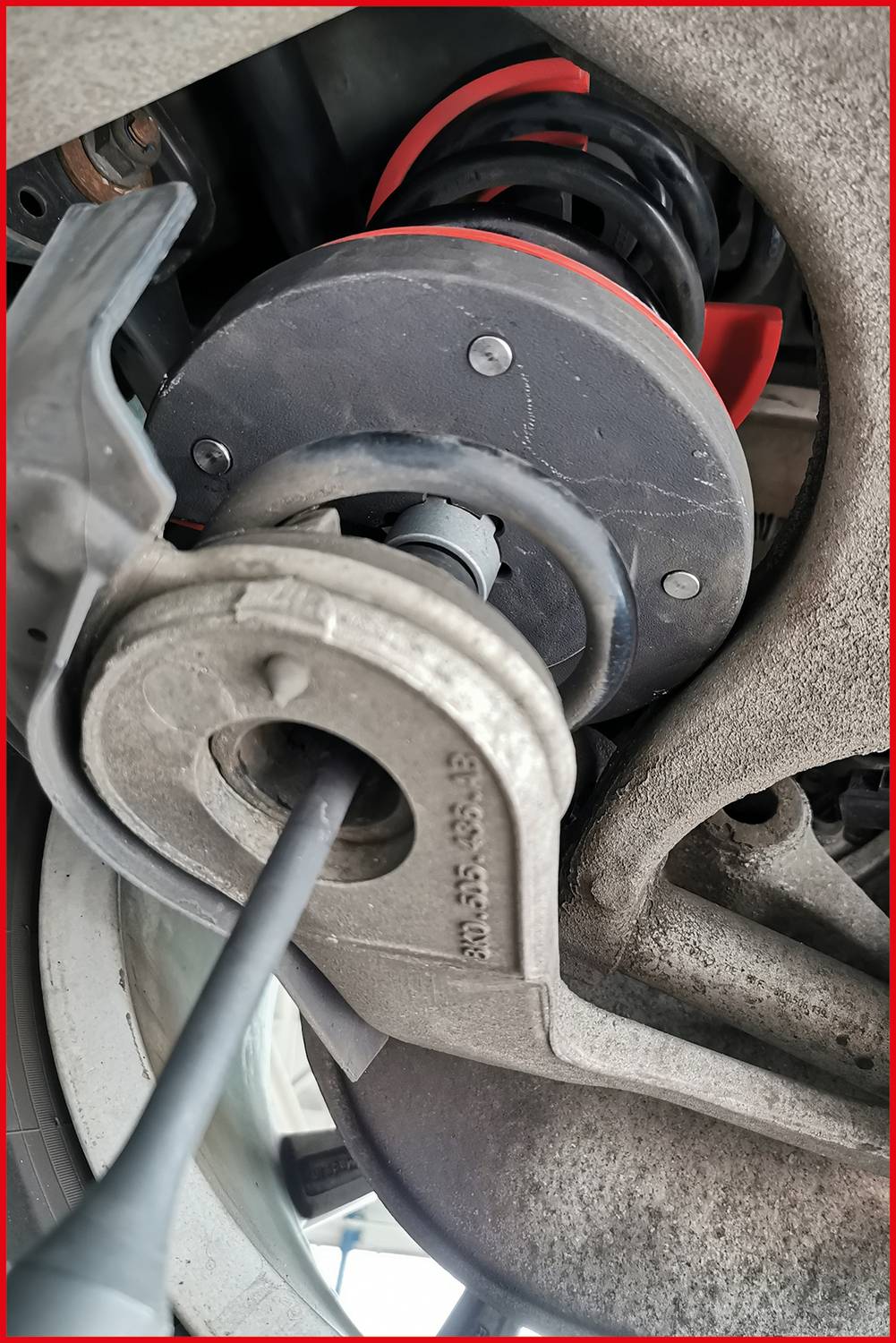 Detailansicht eines Autostoßdämpfers in einer Werkstatt. Technische Komponente mit Schrauben, Federn und Aufhängungselementen sichtbar.