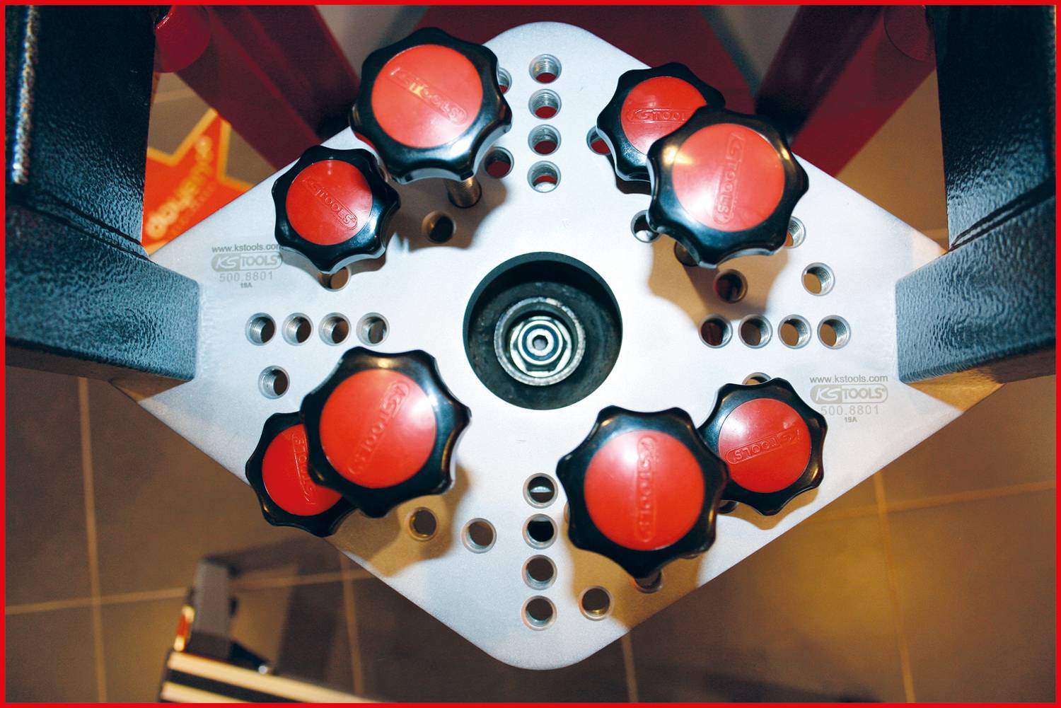 Werkzeug mit acht roten Drehgriffen auf silberner Plattform; ansicht von oben. Werkzeug vermutlich für Präzisions- oder Einstellungszwecke.