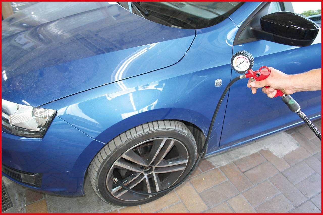 Ein Auto in blauer Farbe wird gewartet, indem Luft in den vorderen Reifen gepumpt wird. Eine Hand hält ein Druckmessgerät.