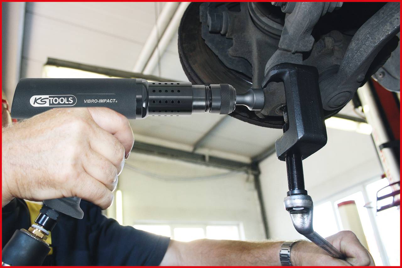 Eine Person benutzt ein pneumatisches Werkzeug, um einen Schraubendreher an einer Autoteil-Befestigung anzuziehen; Fokus auf Werkzeug und Hand.