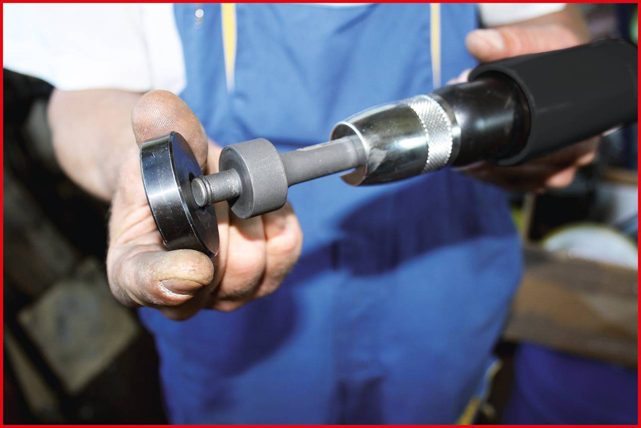 Ein Mensch in blauer Arbeitskleidung hält ein Schleifwerkzeug in den Händen, vermutlich bei der Arbeit in einer Werkstatt.