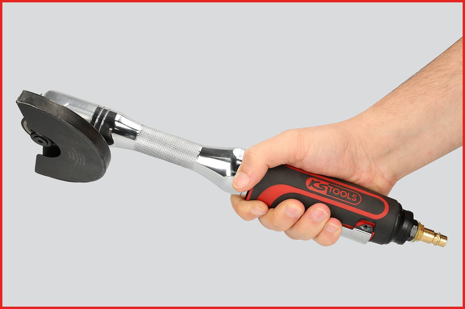 Eine Hand hält ein pneumatisches Werkzeug, das einem Winkelschleifer ähnelt. Es hat einen roten und schwarzen Griff mit 'KS TOOLS' Aufschrift.