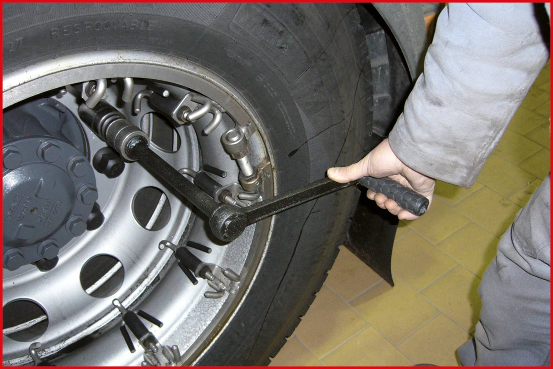 Ein Mechaniker zieht die Schrauben eines Lkw-Reifens mit einem Drehmomentschlüssel an. Der Reifen befindet sich in einer Werkstatt.