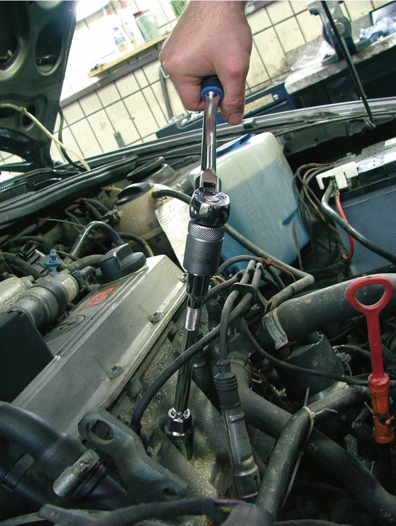 Eine Person zieht mit einem Drehmomentschlüssel Schrauben im Motorraum eines Autos an.