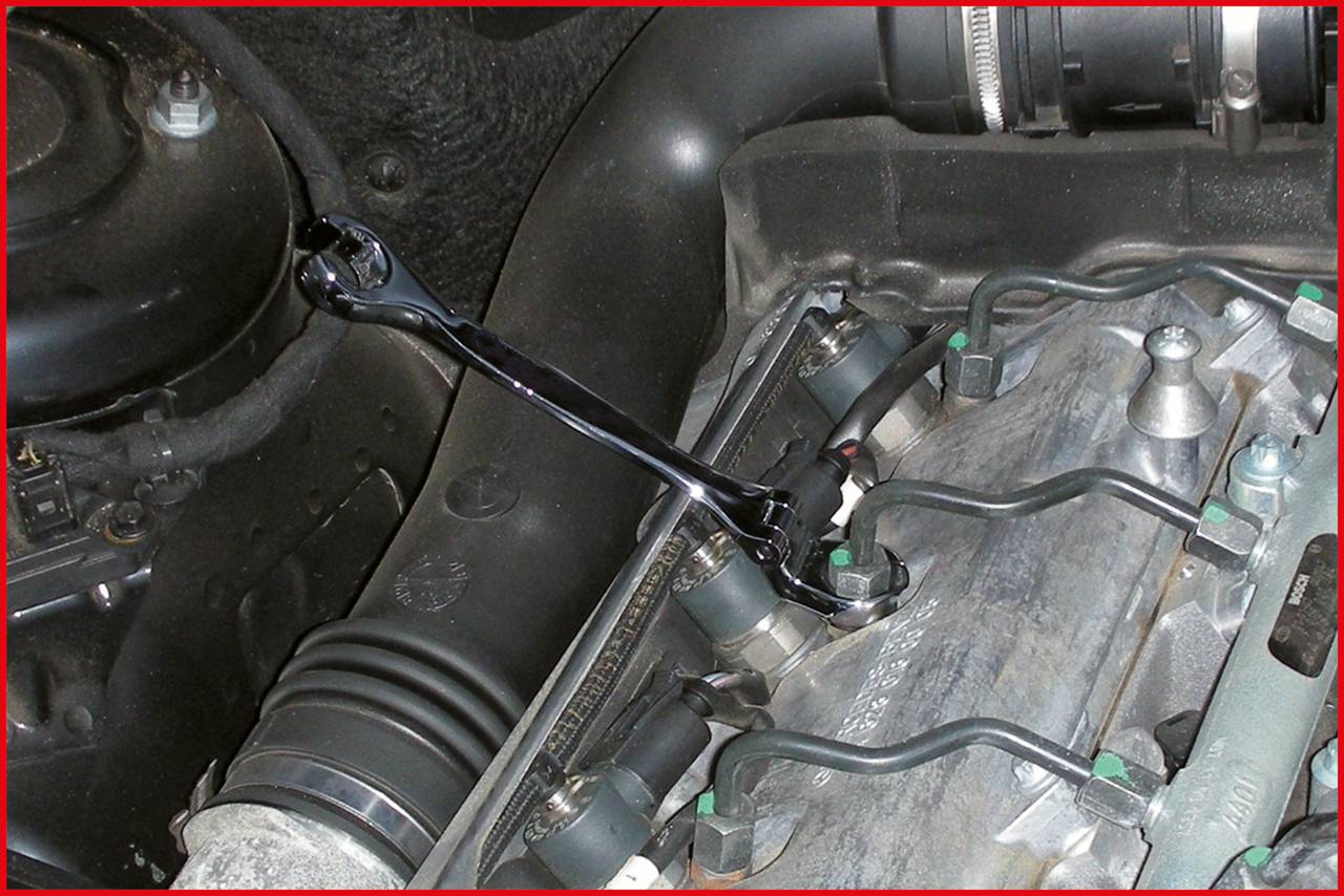 Ein Schraubenschlüssel wird verwendet, um einen Zündkerzenkopf in einem Motorraum zu lösen oder festzuziehen.
