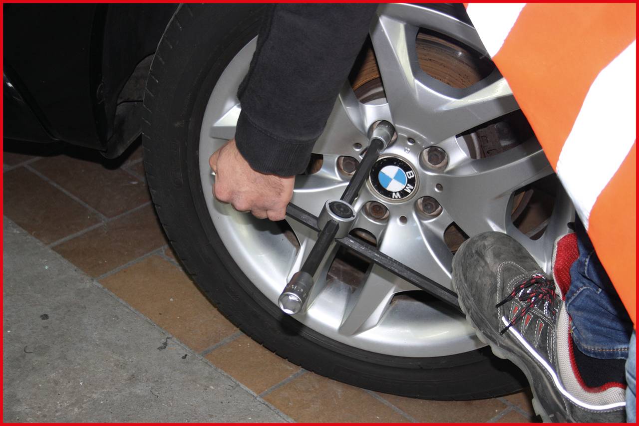 Eine Person zieht die Schrauben eines Autoreifens mit einem Radkreuz an. Die Felge hat ein markantes Logo in der Mitte.