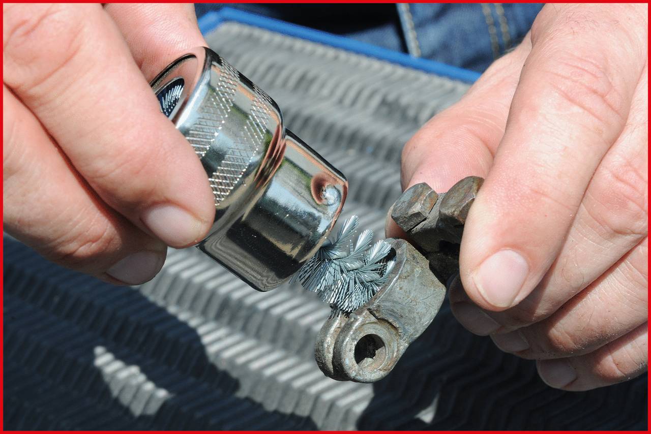 Person reinigt ein metallisches Objekt mit einer Drahtbürste. Nahaufnahme zeigt Detailarbeit auf geriffelter Unterlage.