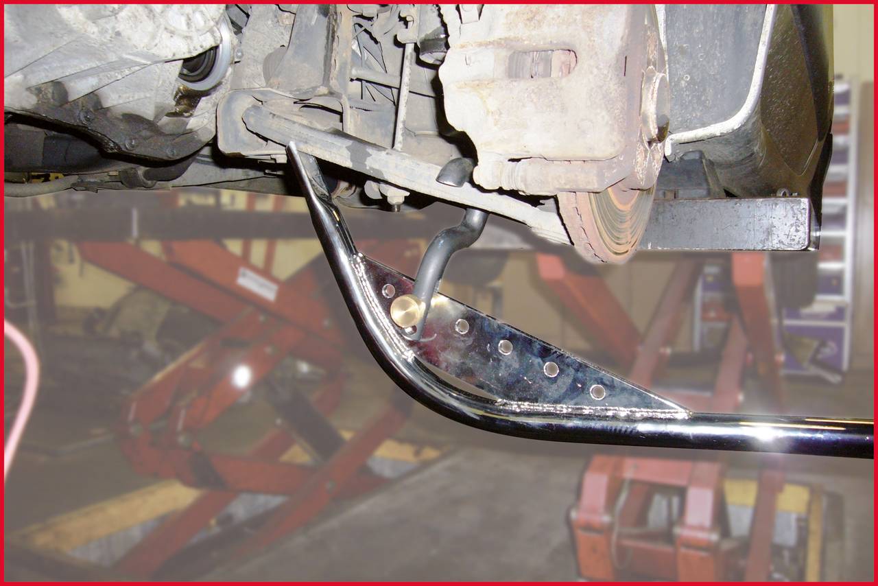 Ein Auto ist auf einer Hebebühne, ein Metallteil wird repariert oder montiert. Im Hintergrund sind Autoreparaturwerkzeuge sichtbar.