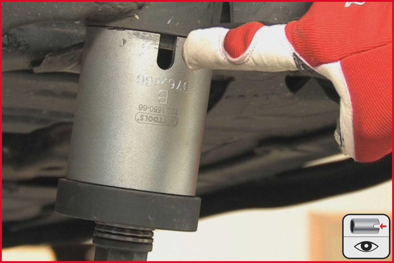 Reifenwechsel: Eine Person zeigt auf einen speziellen Adapter am Wagenheber, der unter einem Fahrzeug positioniert ist.