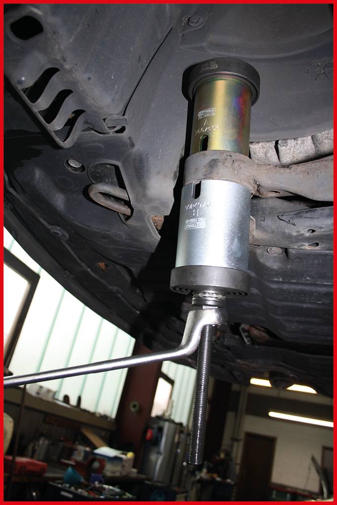 Ein Federspanner-Tool wird verwendet, um die Federn an einem Auto aufzuspannen. Die Szene spielt in einer Autowerkstatt.