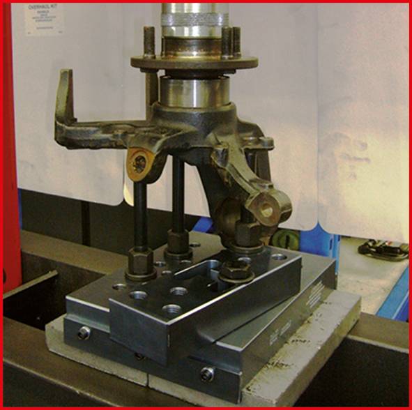Eine Metallvorrichtung mit Hebelarmen auf einer Werkbank. Sie wird wahrscheinlich für mechanische Arbeiten oder Tests verwendet.
