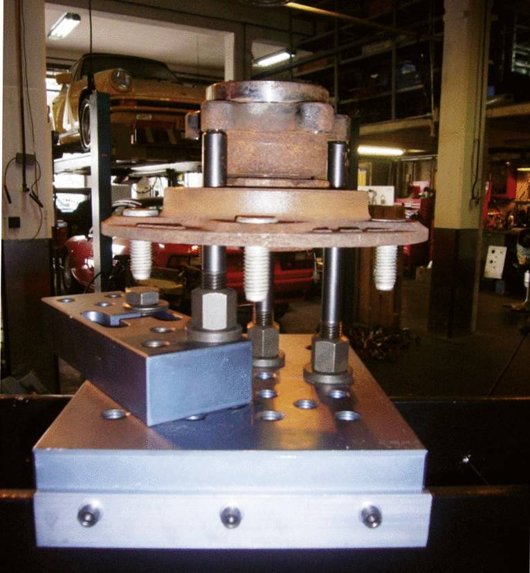 Montage eines Autoteils auf einer Metallvorrichtung in einer Werkstatt. Im Hintergrund sind weitere Autoteile und Werkzeuge zu sehen.