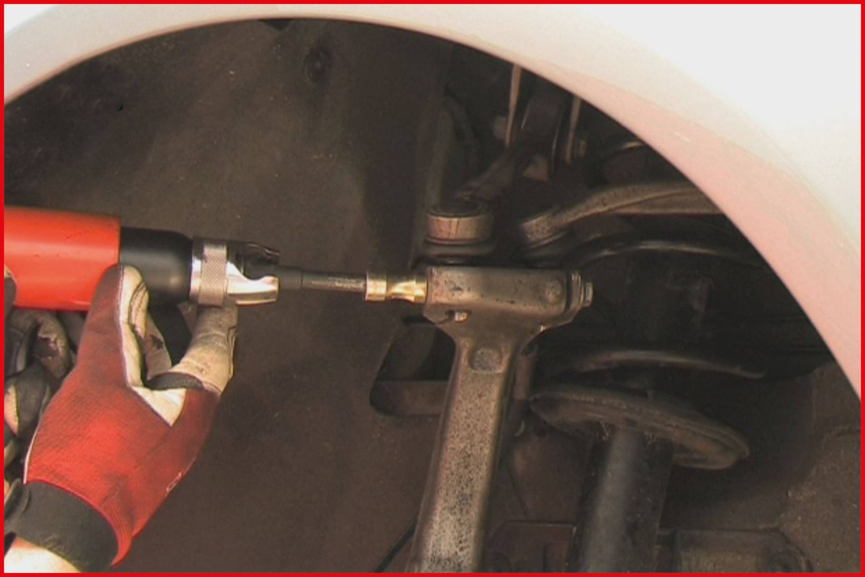 Eine Person repariert oder wartet ein Autoteil mit einem Werkzeug. Das Bild zeigt einen Nahbereich der Federung eines Fahrzeugs.