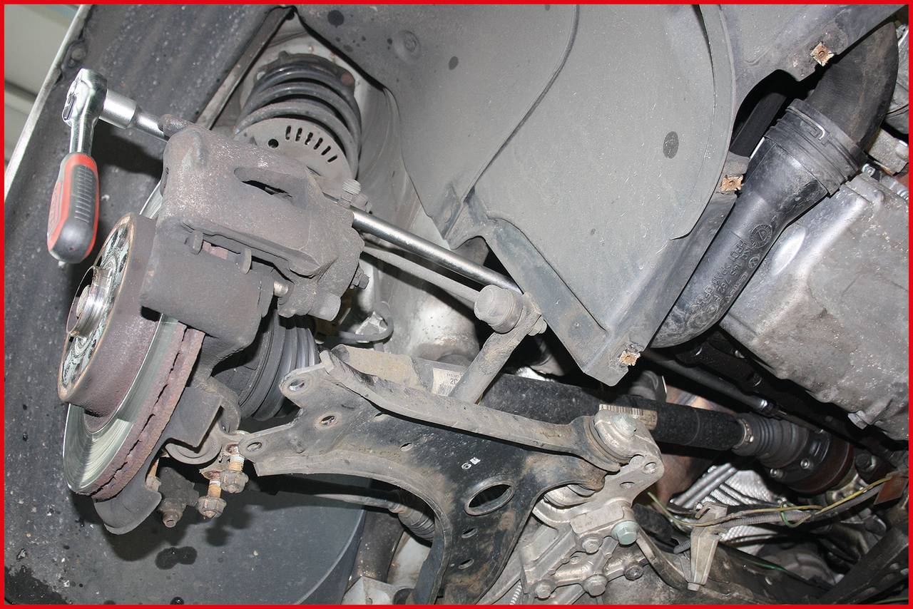 Ein Auto wird von unten repariert. Sichtbar ist das Federbein mit Schraubenschlüssel bei der Arbeit an der Aufhängung.