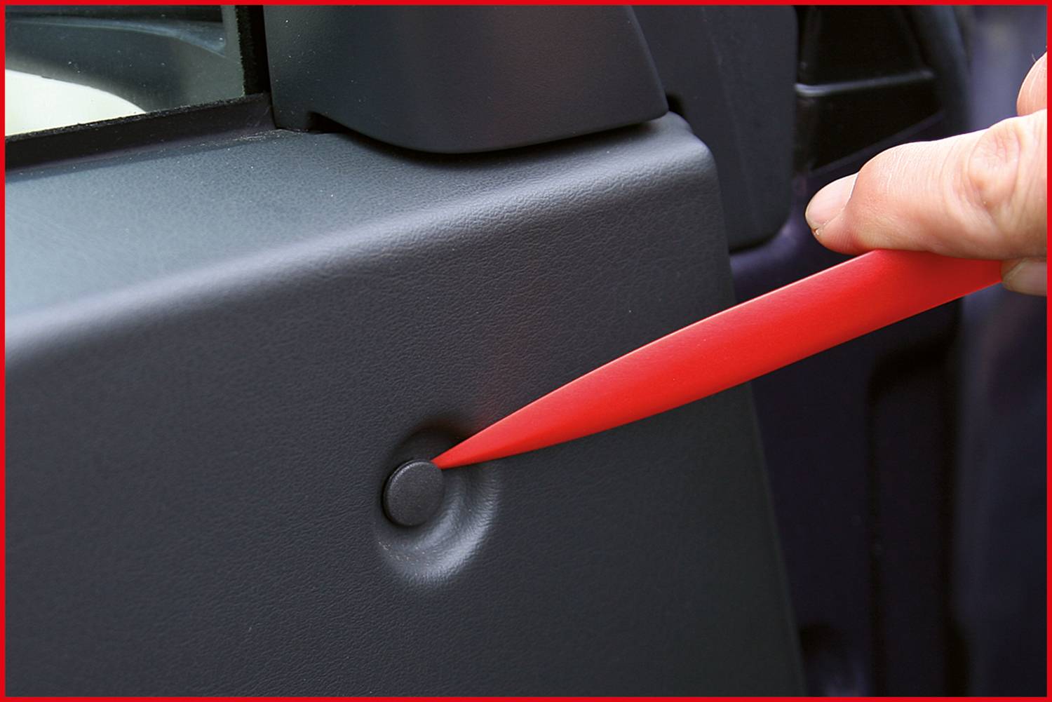 Eine Hand benutzt ein rotes Kunststoffwerkzeug, um vorsichtig eine kleine Kappe an der Autotürabdeckung zu entfernen.