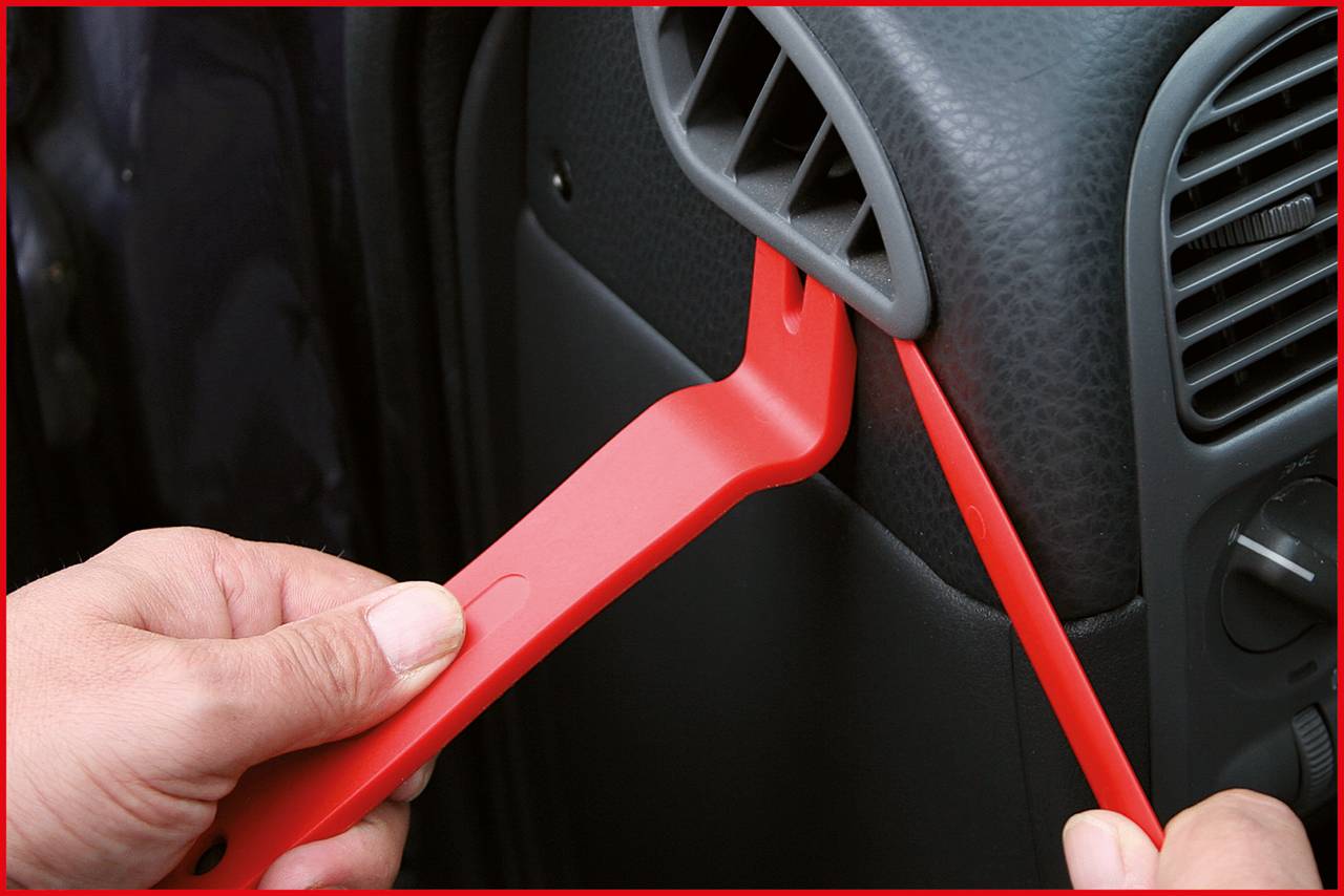 Eine Person benutzt rote Kunststoffwerkzeuge, um eine Autoinnenverkleidung zu entfernen.