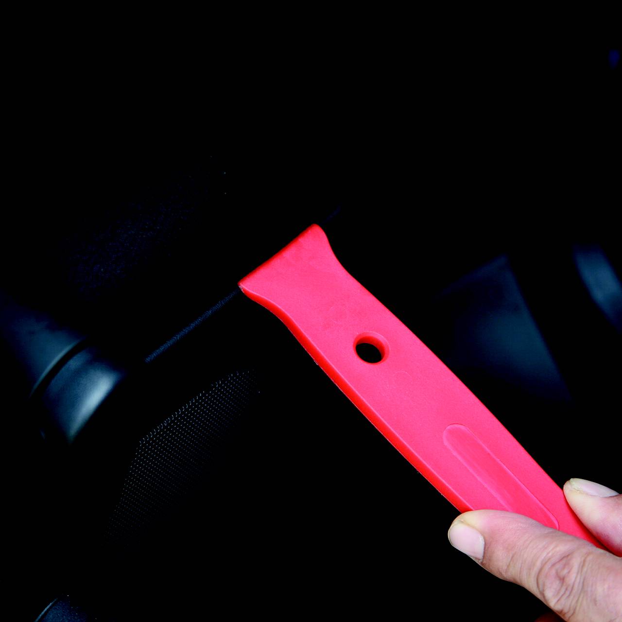 Eine Person hält einen roten Eiskratzer im Auto. Thematik: Wintervorbereitung.