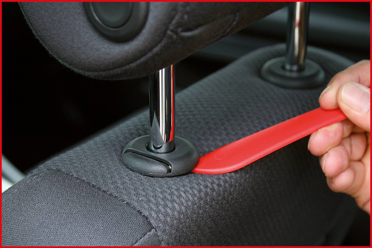 Eine Person benutzt ein rotes Werkzeug, um die Kopfstütze eines Autositzes von der Halterung zu lösen.