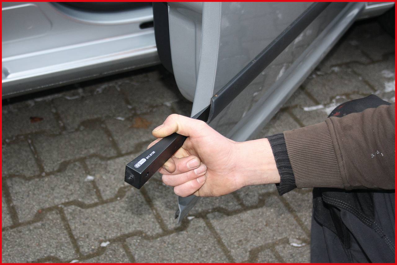 Eine Person hält ein Gerät, das an ein offenes Autotürschloss angebracht ist. Das Gerät scheint ein Türschloss-Öffner zu sein.