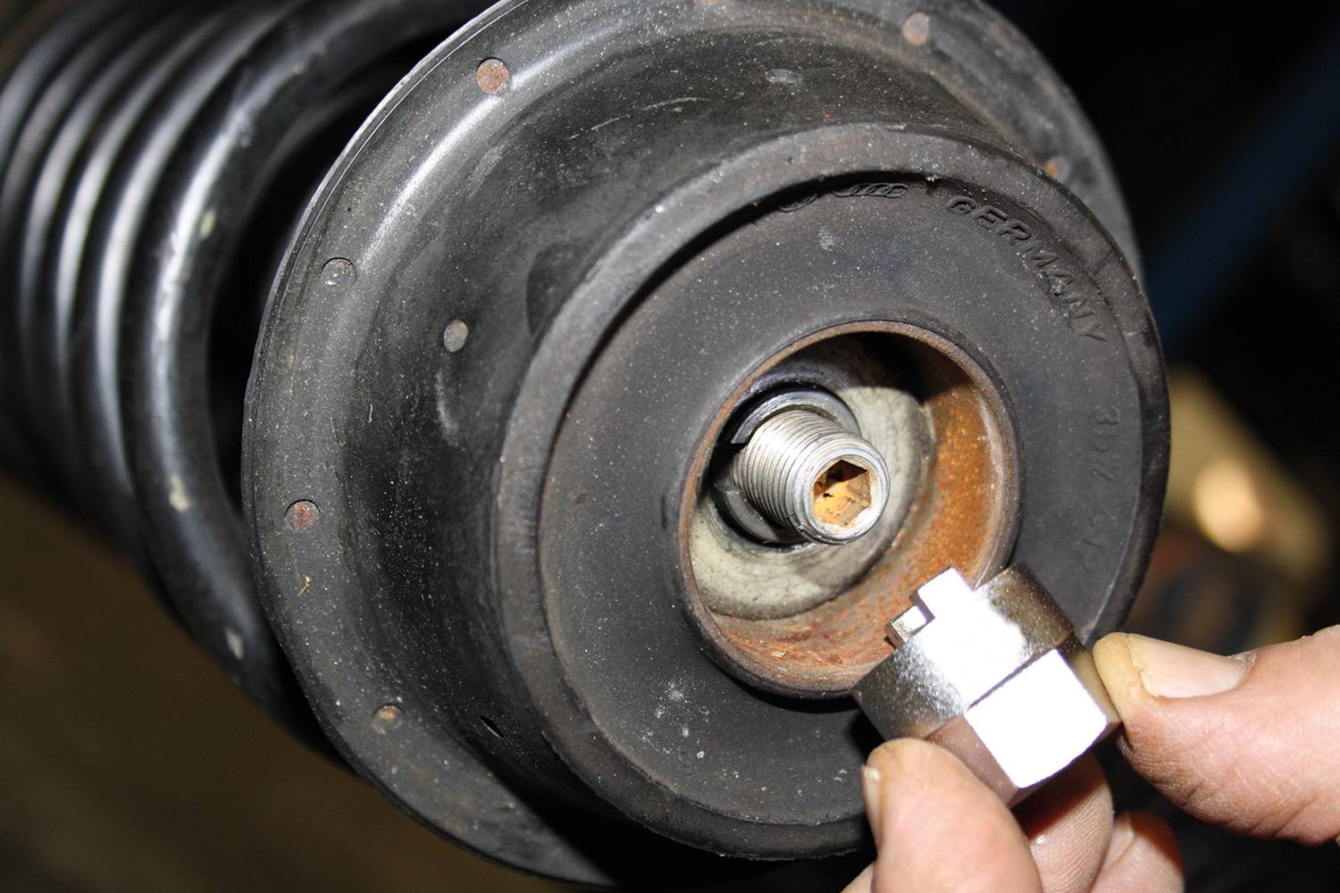 Close-up auf eine Autoteil, das die Federbeinaufnahme mit einer Person zeigt, die einen speziellen Aufsatz für die Reparatur hält.