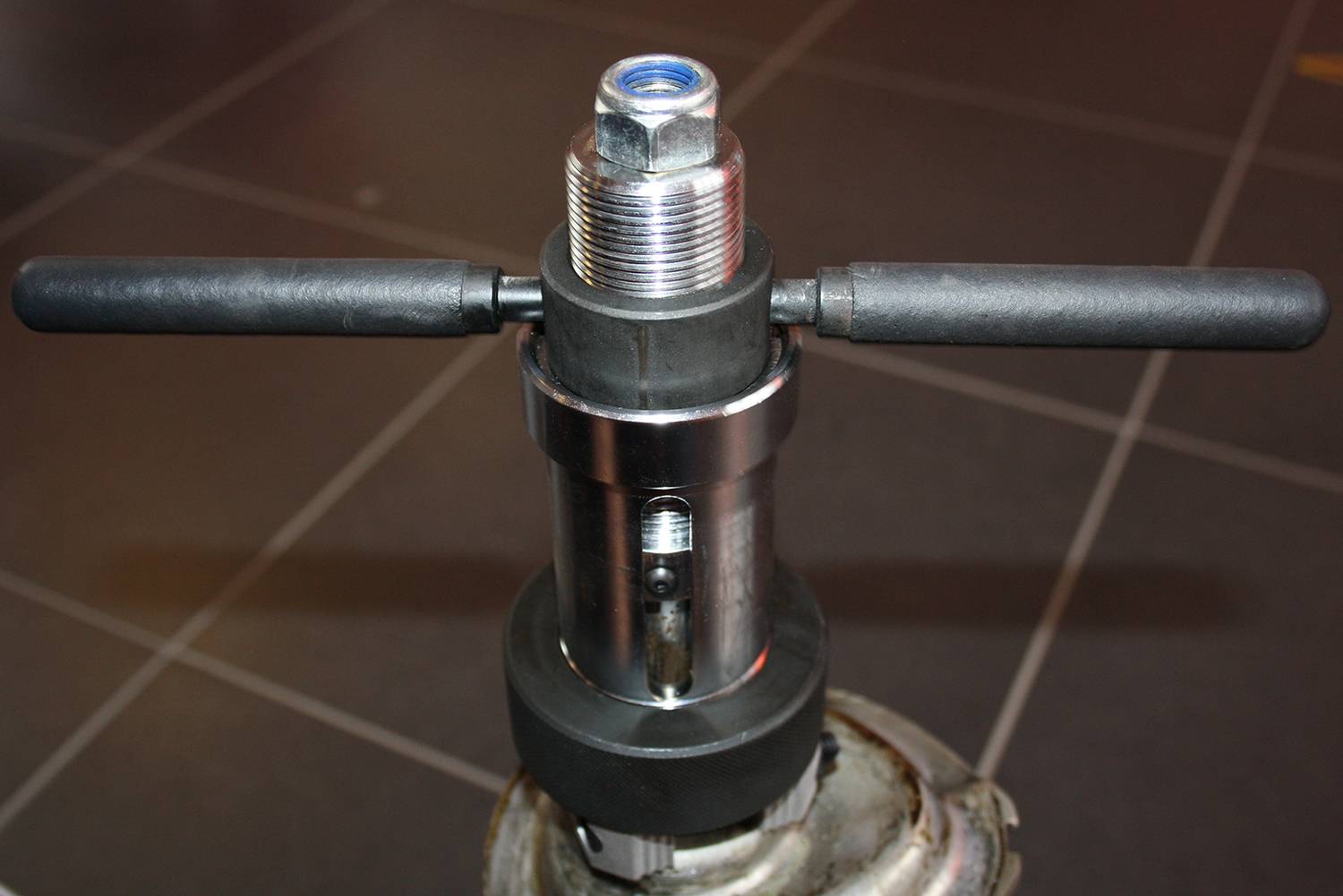 Ein Metallwerkzeug mit zwei Griffen, das auf einem Fliesenboden steht. Es scheint ein manuelles Gerät zur Rohrbearbeitung zu sein.