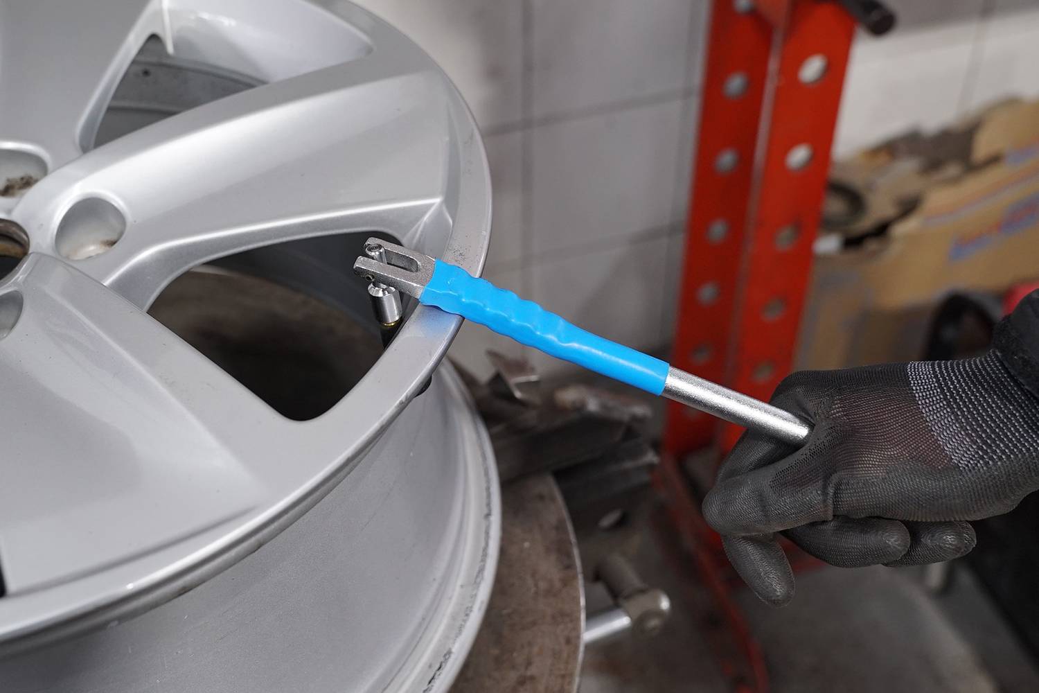 Eine Person zieht mit einem blauen Drehmomentschlüssel an einer Schraube auf einer silbernen Autoreifenfelge in einer Werkstatt an.