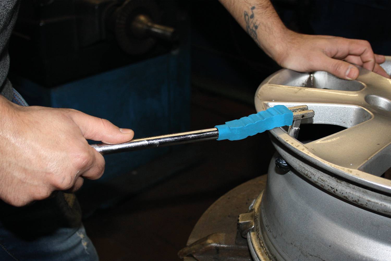 Eine Person zieht mit einem Drehmomentschlüssel die Schrauben einer Autoreifenfelge fest. Handschutz ist sichtbar.